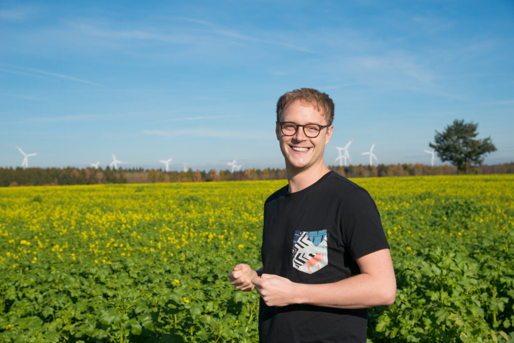 Marcel Emmerich steht in einem Feld im Wahlkreis im Alb-Donau-Kreis. Im Hintergrund sind Windräder zu sehen.